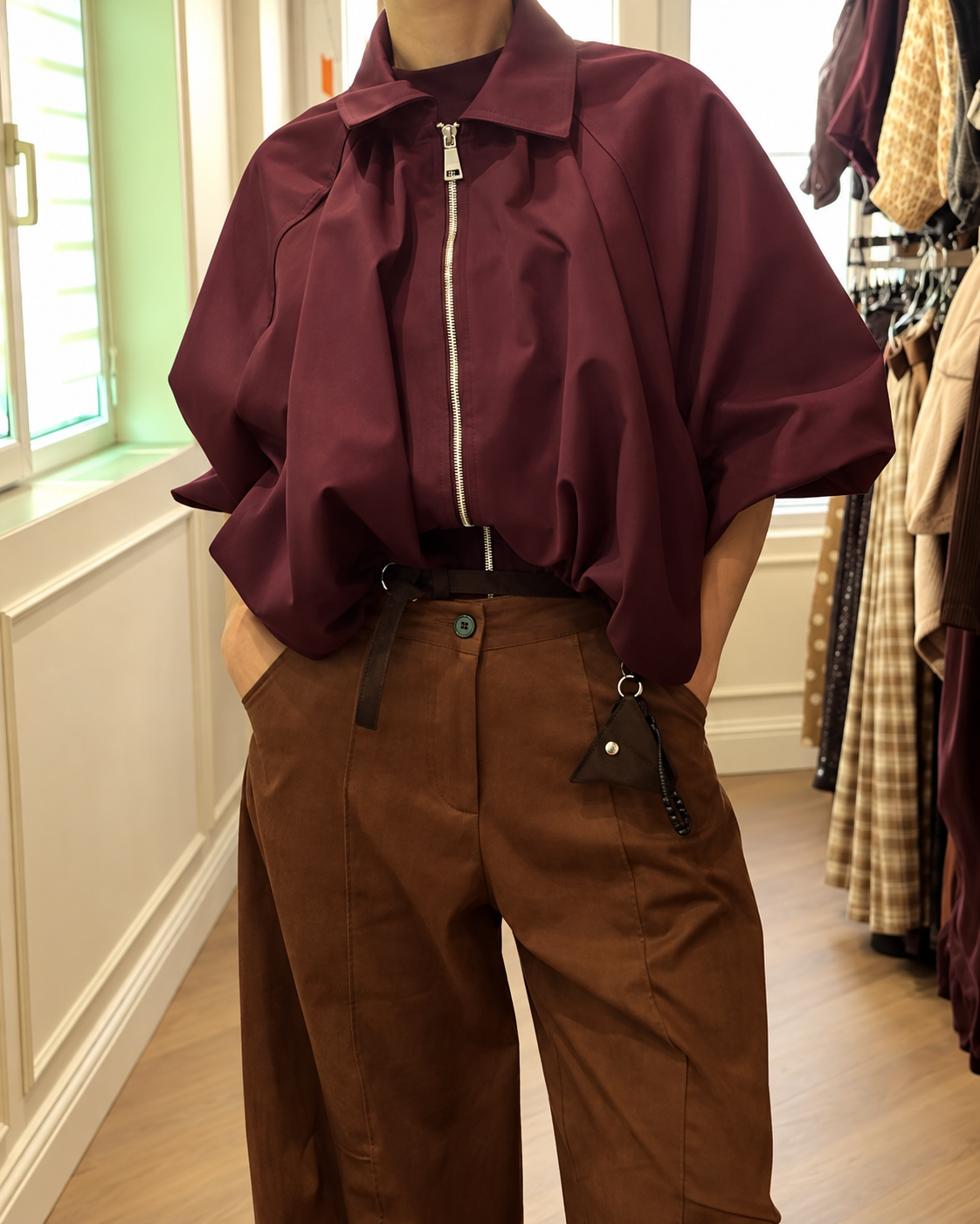 Geacă damă burgundy bordo oversized, cu fermoar, guler amplu și mâneci suflecate, purtată cu pantaloni maro.